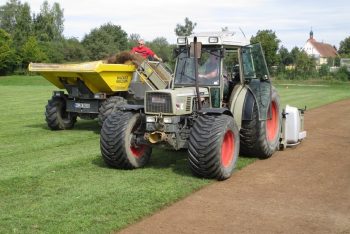 Traktor mit Koro-Fräse trägt Grasnarbe von Rasenspielfeld ab